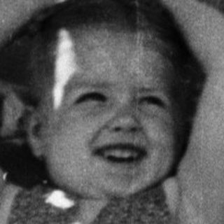 Here's a brief summary of the image: Child sits in a chair, hands behind head, smiling.