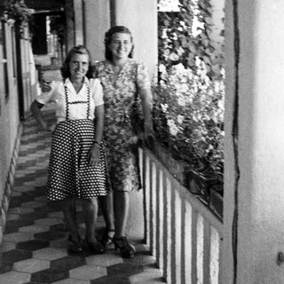 Two women stand on a tiled balcony, partially shaded.