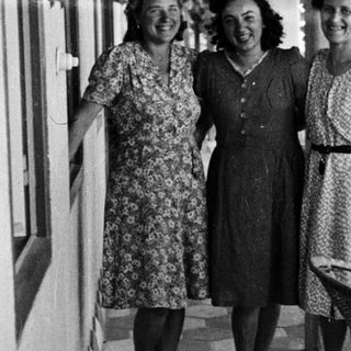Three women in dresses stand on a tiled patio.