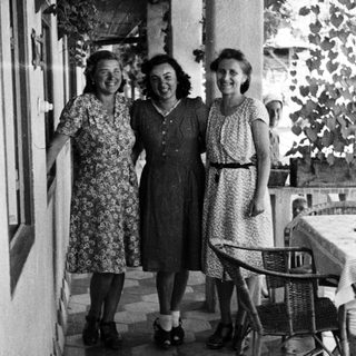 Three women in dresses stand on a tiled patio.