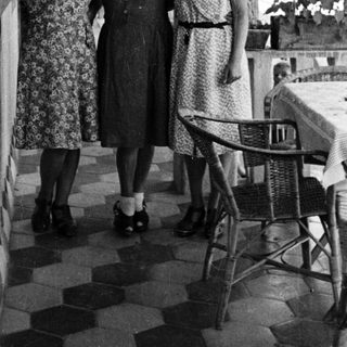Three women in dresses stand on a tiled patio.
