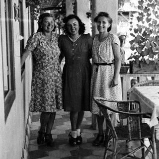 Three women in dresses stand on a tiled patio.