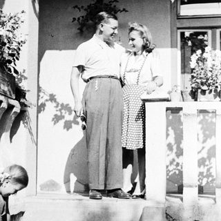 Couple stands on steps, a child nearby, vintage style.