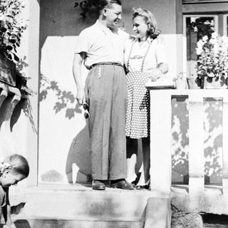 Couple stands on steps, a child nearby, vintage style.