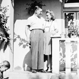 Couple stands on steps, a child nearby, vintage style.