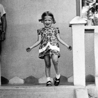 Young girl descends steps, smiling, in vintage clothing.