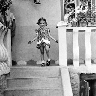 Young girl descends steps, smiling, in vintage clothing.