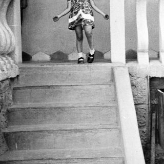 Young girl descends steps, smiling, in vintage clothing.