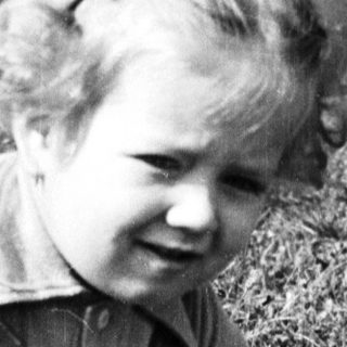Here's a brief summary of the image: Child crouches in grass, appearing to examine something.