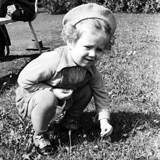 Here's a brief summary of the image: Child crouches in grass, appearing to examine something.
