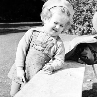 Here's a brief summary of the image: Black and white photo of a young child in overalls.