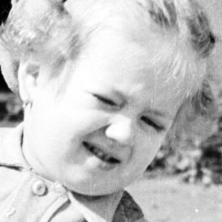 Here's a brief summary of the image: Black and white photo of a young child in overalls.