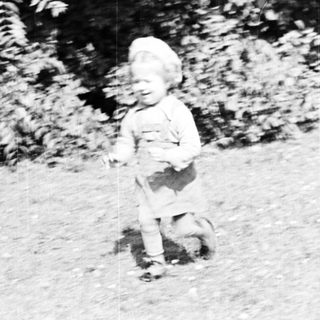 Here's a brief summary of the image: Baby running on grass in front of foliage.