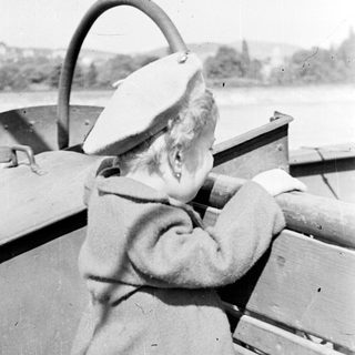 Person wearing a hat steers a boat on water.
