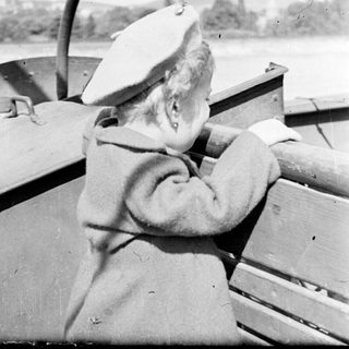 Person wearing a hat steers a boat on water.