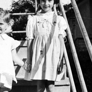 Three young girls stand on stairs in vintage clothing.