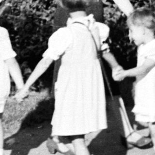 Children holding hands with a woman outdoors.