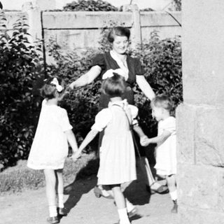 Children holding hands with a woman outdoors.