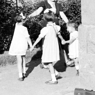 Children holding hands with a woman outdoors.