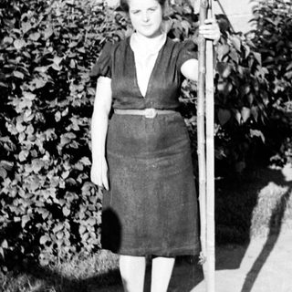 Woman stands holding a small tree in a garden.