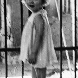 Young child stands near a gate, black and white photo.