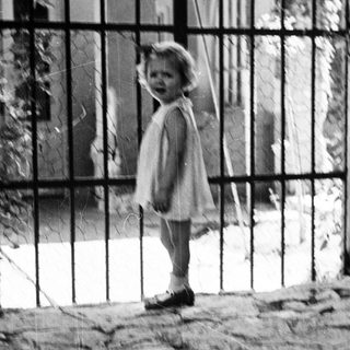 Young child stands near a gate, black and white photo.