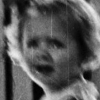 Young child stands near a gate, black and white photo.