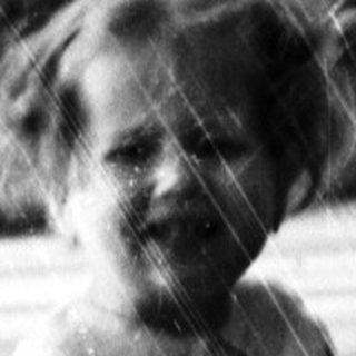 Here's a brief summary of the image: Young child stands outdoors in a vintage dress and boots.
