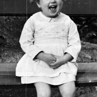 Here's a brief summary of the image: Young girl in a dress sits on a bench.