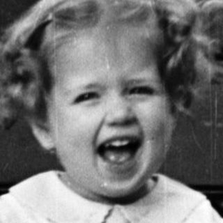 Here's a brief summary of the image: Young girl in a dress sits on a bench.