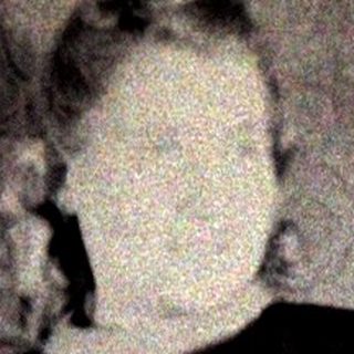 Woman in dress stands near a chair, posing for photo.