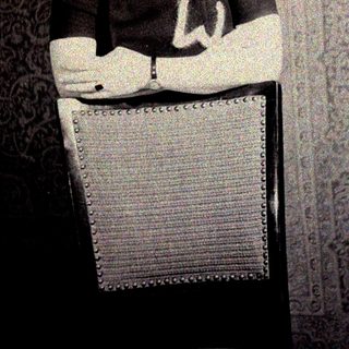 Man seated, wearing a dark shirt, against a patterned wall.