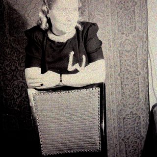 Man seated, wearing a dark shirt, against a patterned wall.
