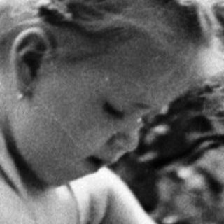 Child pours water from a bucket into a stream.