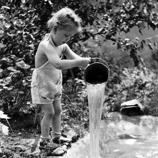Child pours water from a bucket into a stream.