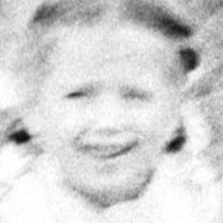Here's a brief summary of the image: Child sits on grass, holding a doll.