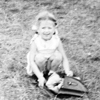 Here's a brief summary of the image: Child sits on grass, holding a doll.