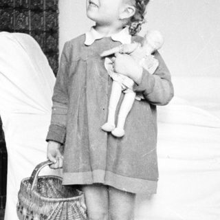 Young girl stands holding a doll and basket.