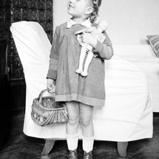 Young girl stands holding a doll and basket.