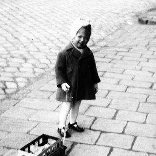 Child pulls a crate on a cobblestone street.