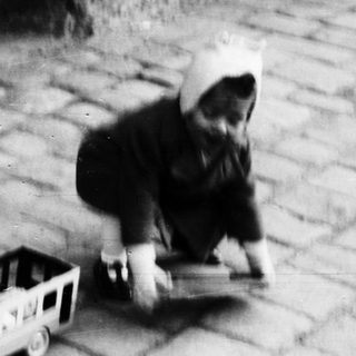 Child plays with a toy cart on a stone path.