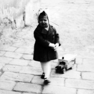 Here's a brief summary of the image: Child in coat walks along a stone-paved surface.