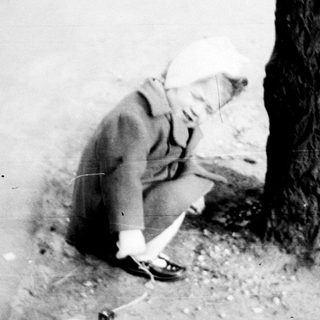 Child sits near a tree, appears to be drawing.