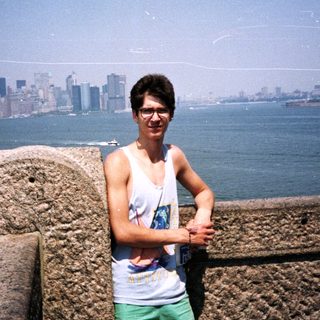 Person poses near water with New York City skyline.