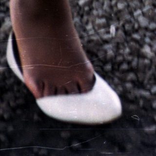 Feet in shoes near a table and rope on gravel.