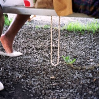 Feet in shoes near a table and rope on gravel.