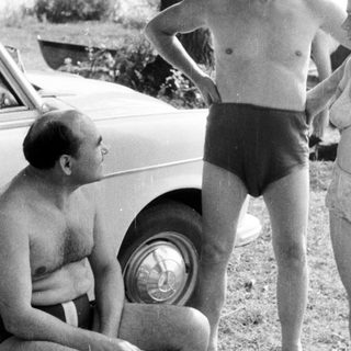 Men and women near a car, appearing to converse.