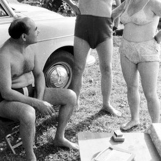 Men and women near a car, appearing to converse.