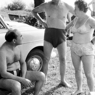 Men and women near a car, appearing to converse.