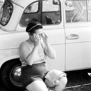 Woman sits near a car, applying cream to her face.